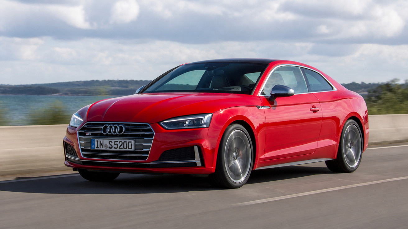 Carro desportivo Audi vermelho circulando numa estrada junto ao mar em dia nublado.